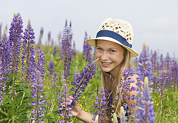 Austria, Teenage girl holding lupine flower, smiling, portrait - WWF002225
