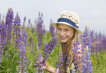 Österreich, Jugendliches Mädchen hält Lupinenblüte, lächelnd, Porträt - WWF002225