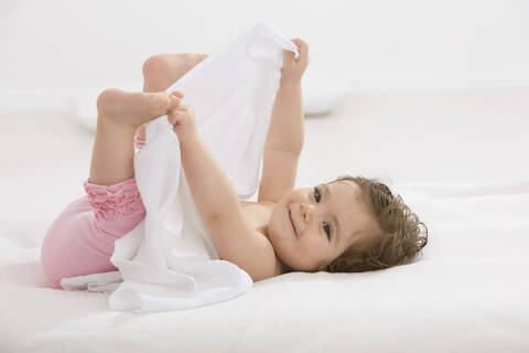 Baby-Mädchen liegt auf dem Rücken und hält Zehen, lächelnd, lizenzfreies Stockfoto