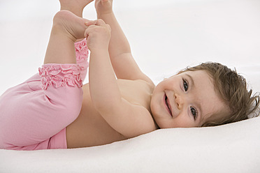 Baby-Mädchen liegt auf dem Rücken und hält Zehen, lächelnd - SMOF000461