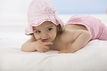 Baby girl lying on blanket with finger in mouth - SMOF000474