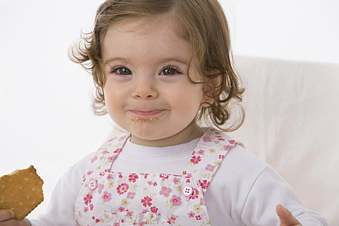 Kleines Mädchen isst Keks, lächelnd, Nahaufnahme - SMOF000497