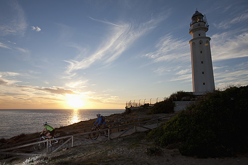 Spanien, Andalusien, Mann und Frau fahren mit dem Fahrrad am Leuchtturm bei Sonnenuntergang - DSF000275