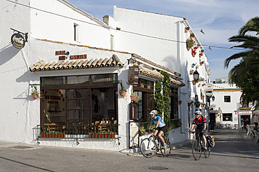 Spain, Andalusia, Conil de la Frontera, Man and woman cycling through street - DSF000285