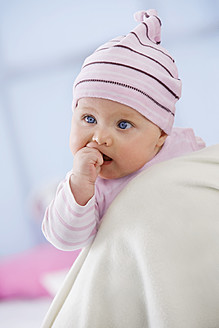 Baby girl in woolly hat with finger in mouth, close up - SMOF000513