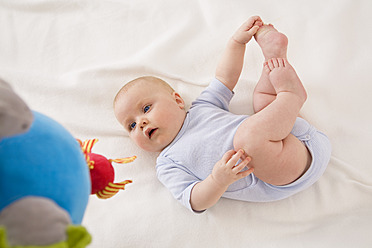 Baby girl lying on baby blanket with holding foot - SMOF000525