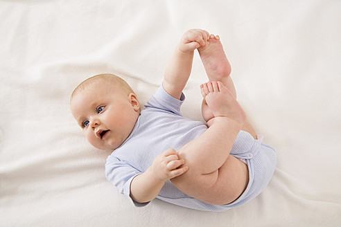 Baby girl lying on baby blanket with holding foot - SMOF000526