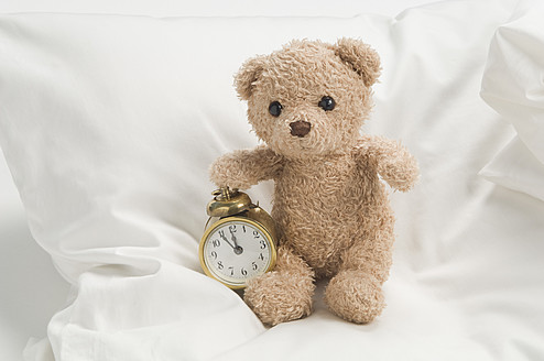 Teddybär mit Wecker auf dem Bett - CRF002119