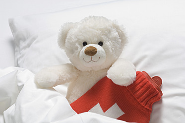 Teddybär mit Wärmflasche auf dem Bett - CRF002118