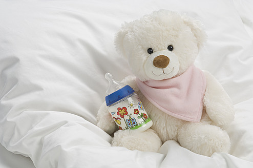 Teddybär mit Milchflasche auf dem Bett - CRF002117