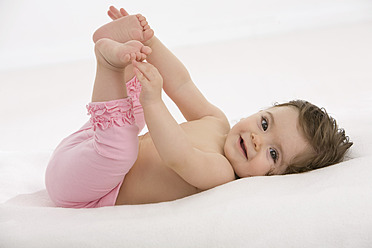 Baby-Mädchen liegt auf dem Rücken und hält Zehen, lächelnd - SMOF000501