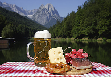 Deutschland, Oberbayern, Bayerische Brotzeit auf Tisch, Berg mit See im Hintergrund - TCF002285