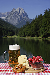 Deutschland, Oberbayern, Bayerische Brotzeit auf Tisch, Berg mit See im Hintergrund - TCF002286