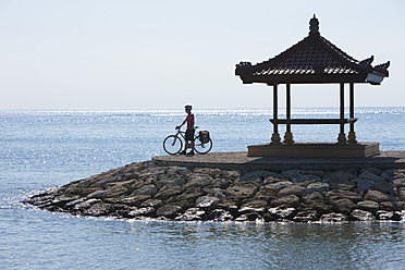 Indonesien, Bali, Sanur, Mann stehend mit Fahrrad in der Nähe Pavillon am Meer - DSF000211