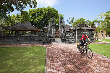 Indonesien, Bali, Kuta, Mann radelt über Fußweg, Tempel im Hintergrund - DSF000300