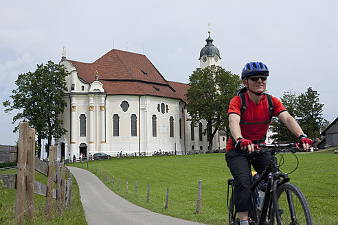 Deutschland, Bayern, Älterer Mann fährt Fahrrad mit Wieskirche im Hintergrund - DSF000223
