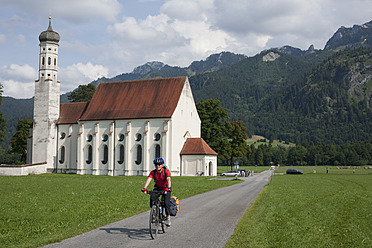 Deutschland, Bayern, Füssen, Älterer Mann fährt Fahrrad mit Kirche im Hintergrund - DSF000283