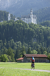 Deutschland, Bayern, Älterer Mann fährt Fahrrad, Schloss Neuschwanstein im Hintergrund - DSF000224