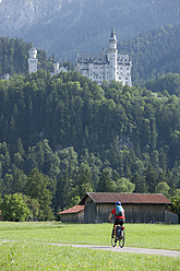 Germany, Bavaria, Mature man riding bicycle, Neuschwanstein Castle in background - DSF000224