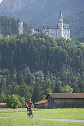 Germany, Bavaria, Mature man riding bicycle, Neuschwanstein Castle in background - DSF000225