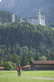 Deutschland, Bayern, Älterer Mann fährt Fahrrad, Schloss Neuschwanstein im Hintergrund - DSF000225