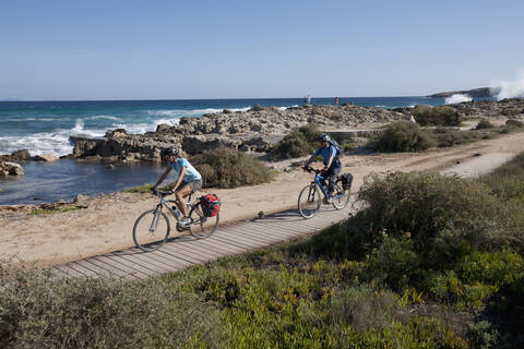 Spanien, Formentera, Älterer Mann und mittlere erwachsene Frau fahren Fahrrad, lizenzfreies Stockfoto