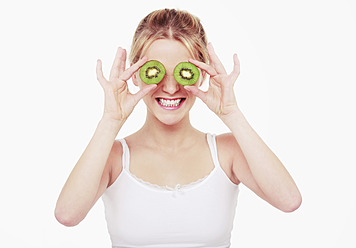 Junge Frau bedeckt ihre Augen mit Kiwi-Stücken und lächelt - WVF000227