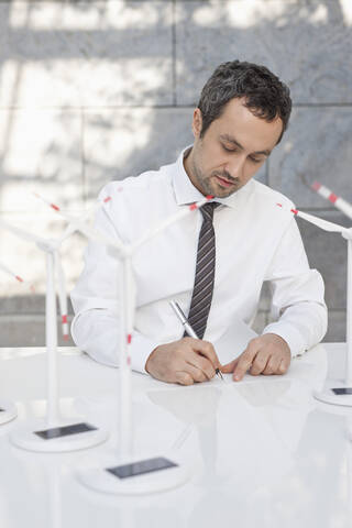 Deutschland, Leipzig, Geschäftsmann mit Windkraftmodell auf dem Schreibtisch, lizenzfreies Stockfoto