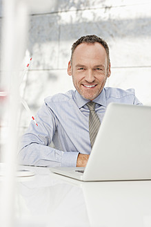 Germany, Leipzig, Businessman using laptop with wind power model - WESTF018512