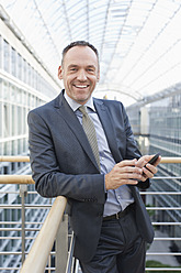 Deutschland, Leipzig, Geschäftsmann mit Mobiltelefon, lächelnd, Porträt - WESTF018556