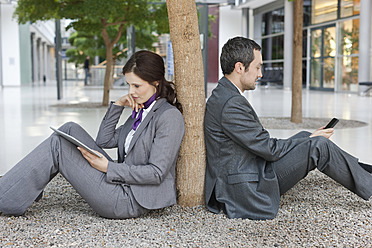 Deutschland, Leipzig, Geschäftsleute sitzen an einem Baum mit digitalem Tablet und Mobiltelefon - WESTF018569