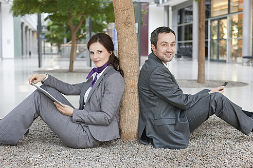 Deutschland, Leipzig, Geschäftsleute sitzen an einem Baum mit digitalem Tablet und Mobiltelefon - WESTF018570