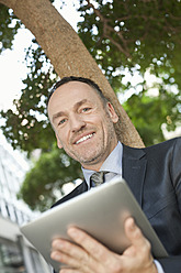 Deutschland, Leipzig, Geschäftsmann sitzend am Baum mit digitalem Tablet - WESTF018574