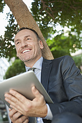 Deutschland, Leipzig, Geschäftsmann sitzend am Baum mit digitalem Tablet - WESTF018575