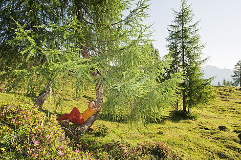 Austria, Salzburg County, Young woman leaning on tree in alpine meadow - HHF004004