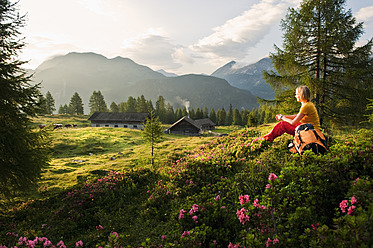 Österreich, Land Salzburg, Junge Frau sitzt auf einer Almwiese und beobachtet die Landschaft - HHF004009