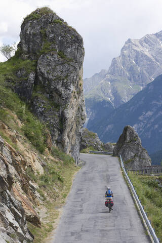 Schweiz, Älterer Mann fährt mit dem Fahrrad durch eine Bergstraße, lizenzfreies Stockfoto