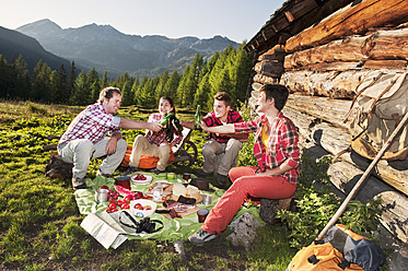 Österreich, Salzburg, Männer und Frauen beim Picknick in der Nähe einer Almhütte bei Sonnenuntergang - HHF004038