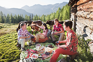 Österreich, Land Salzburg, Männer und Frauen beim Picknick in der Nähe einer Almhütte bei Sonnenuntergang - HHF004036