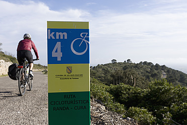 Spain, Mallorca, Woman cycling, road sign in foreground - DSF000406