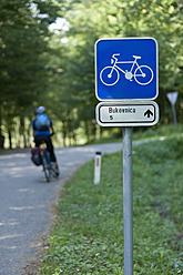 Slovenia, Bukovnica, Mature man cycling beside road sign - DSF000422