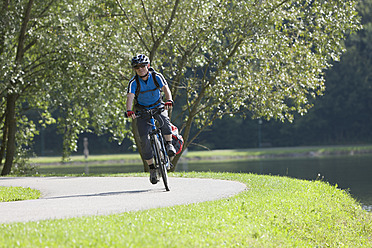 Austria, Mature man riding bicycle beside Lake Stubenberg - DSF000436