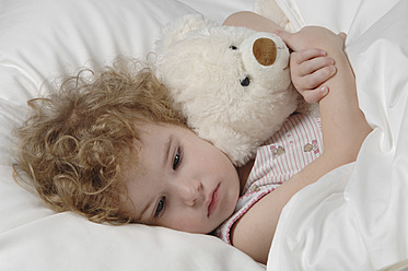 Sick girl lying in bed with teddy bear - CRF002142