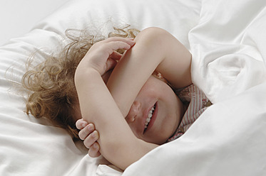 Mädchen liegt auf dem Bett und bedeckt ihre Augen, lächelnd - CRF002145