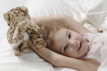 Mädchen mit Spielzeug auf dem Bett liegend, lächelnd - CRF002146