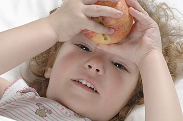 Mädchen auf dem Bett liegend mit Apfel, lächelnd - CRF002150