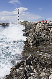 Spanien, Menorca, Mann und Frau sitzen auf einer Klippe, Cap d'Artrutx im Hintergrund - DSF000502