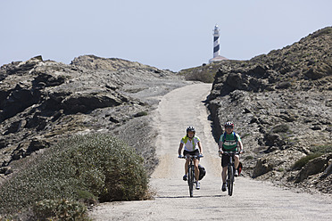 Spanien, Menorca, Mann und Frau beim Radfahren, Cap de Favaritx im Hintergrund - DSF000517