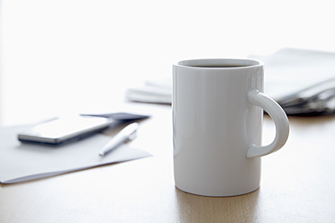 Tasse Kaffee, Zeitung, Mobiltelefon und Stift auf dem Bürotisch, Nahaufnahme - TCF002312