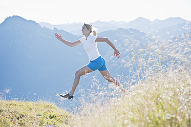 Österreich, Land Salzburg, Junge Frau läuft und springt auf einer Almwiese - HHF004042